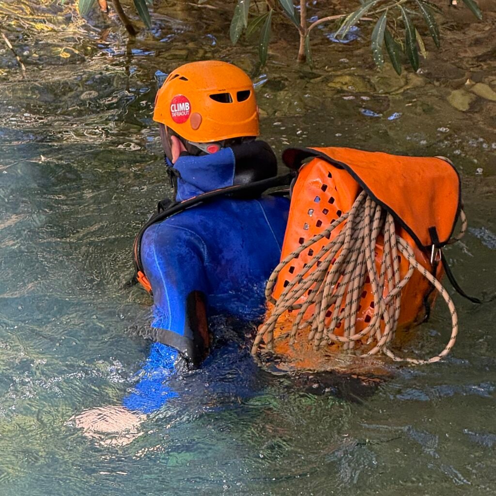 Traveler wearing a helmet and carrying gear swimming through a canyon river in Morocco