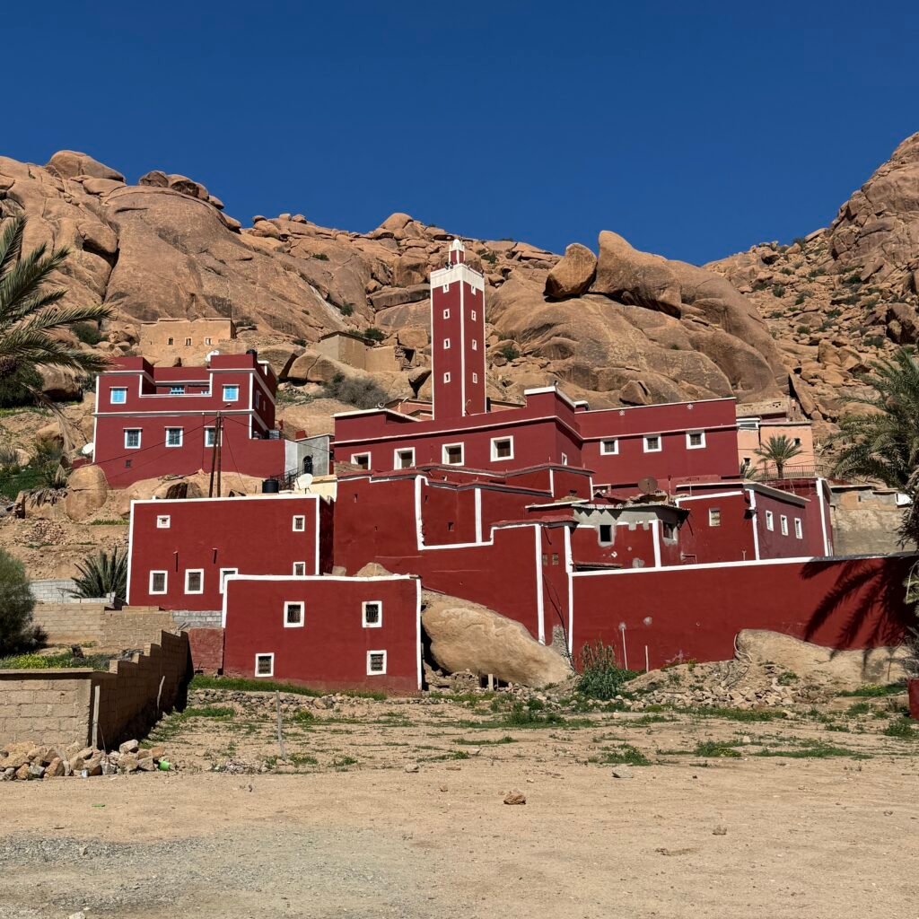 Traditional red building with white trim and a minaret against a rocky mountain in Tafraoute, Morocco