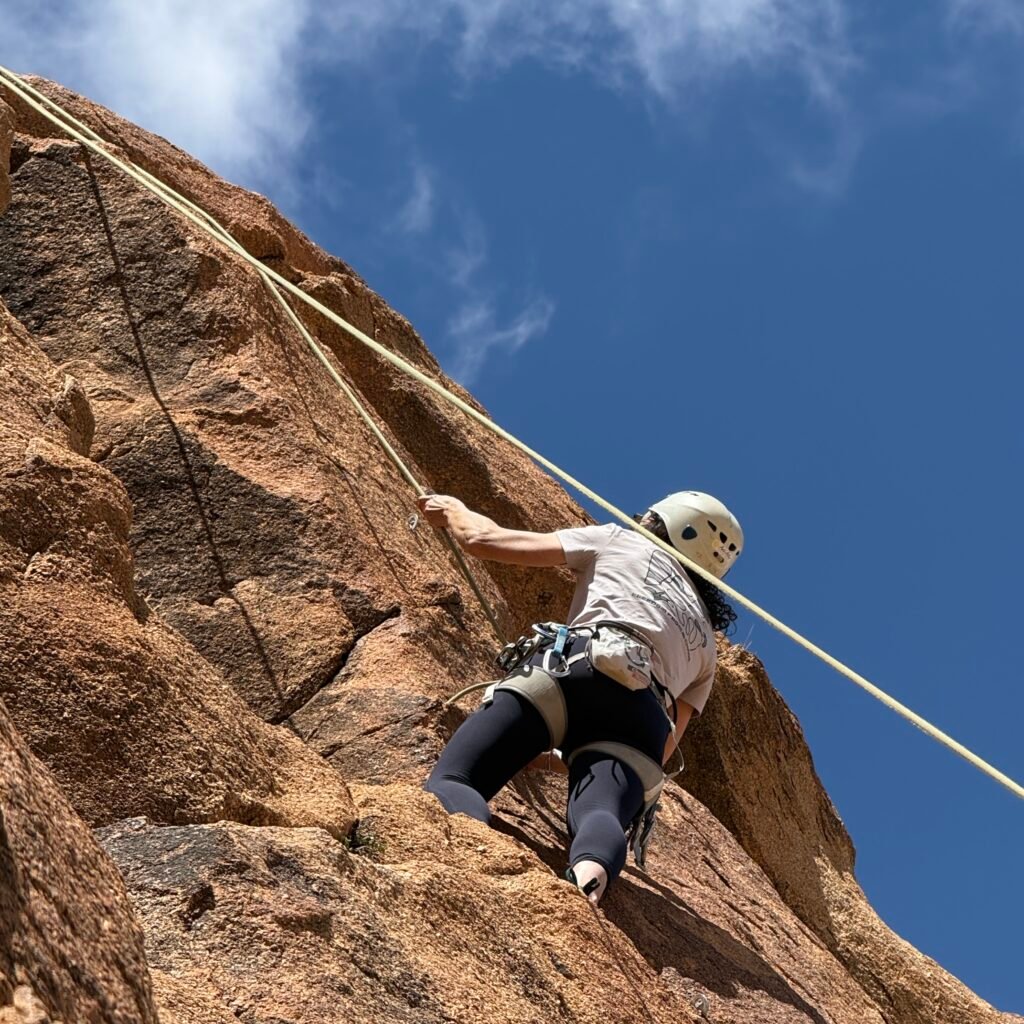 Female climber scaling a sunlit granite cliff face against a blue sky in Morocco