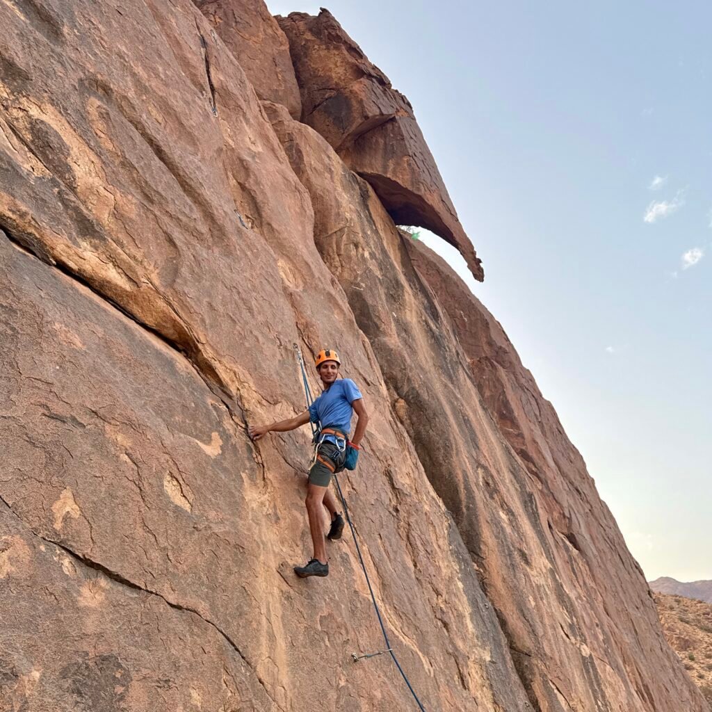 Climber in an orange helmet pausing on a high rock wall route in Morocco