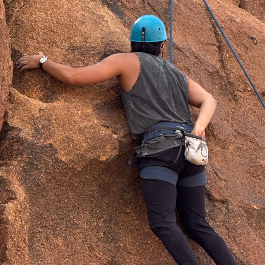 Climber reaching for chalk in a chalk bag while scaling a granite rock in Morocco