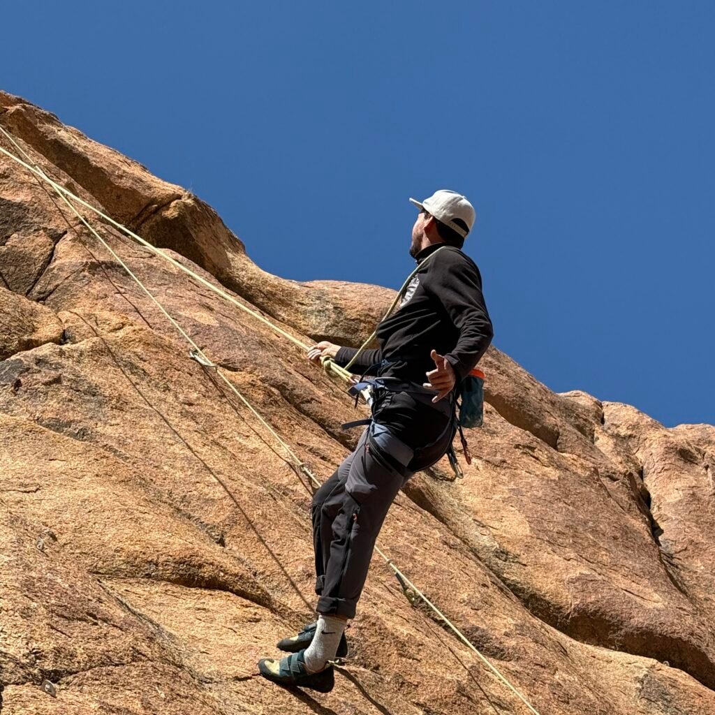 Low-angle view of a climber traversing a steep granite wall under a clear sky in Morocco