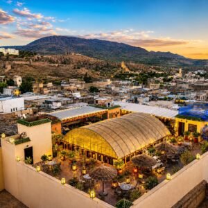 Panoramic view of a town at sunset with rooftops and a restaurant terrace set up with lanterns and seating