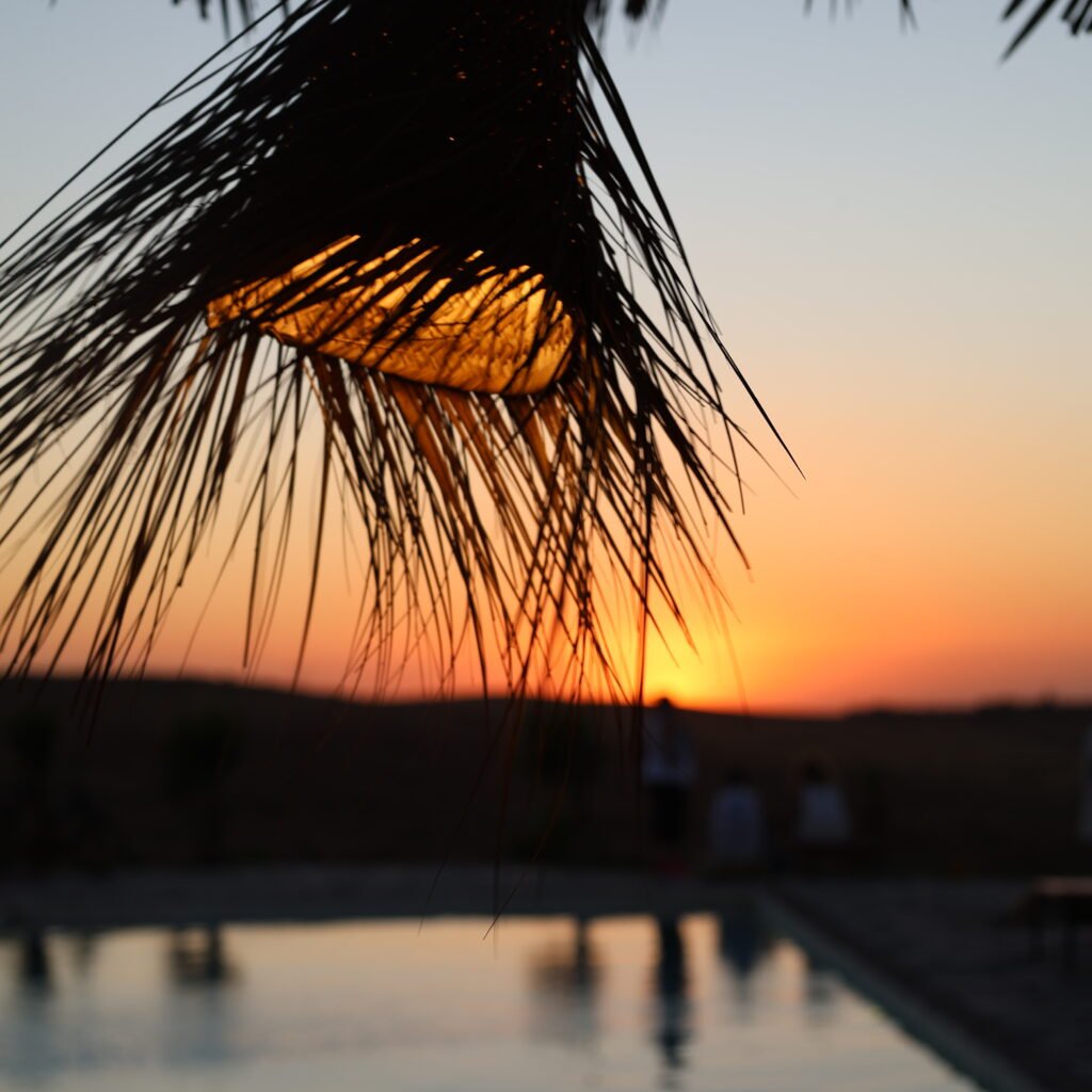 Sunset view through a traditional woven lampshade by a calm swimming pool