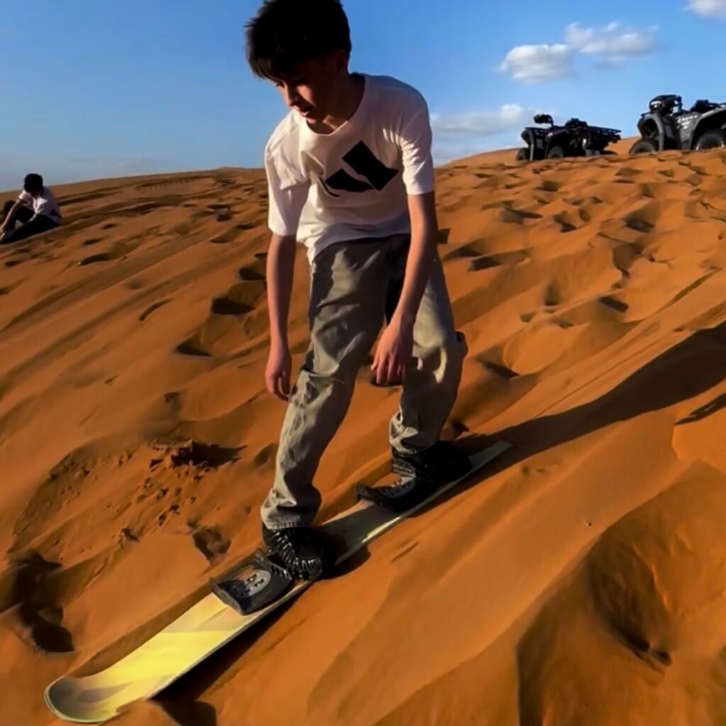 Young boy balancing on a sandboard while sliding down a desert sand dune