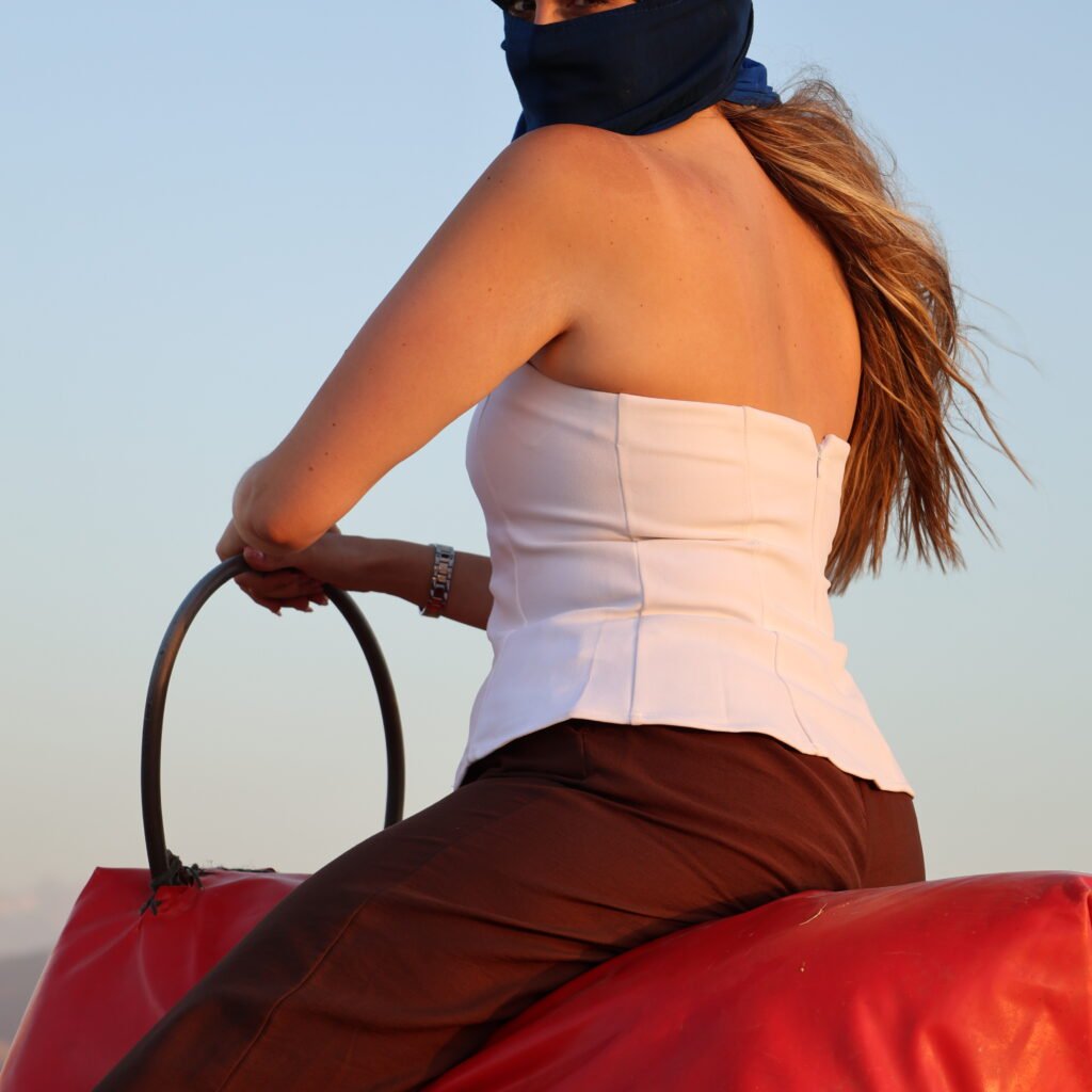 Traveler wrapped in a blue traditional headscarf seated atop a camel at sunset