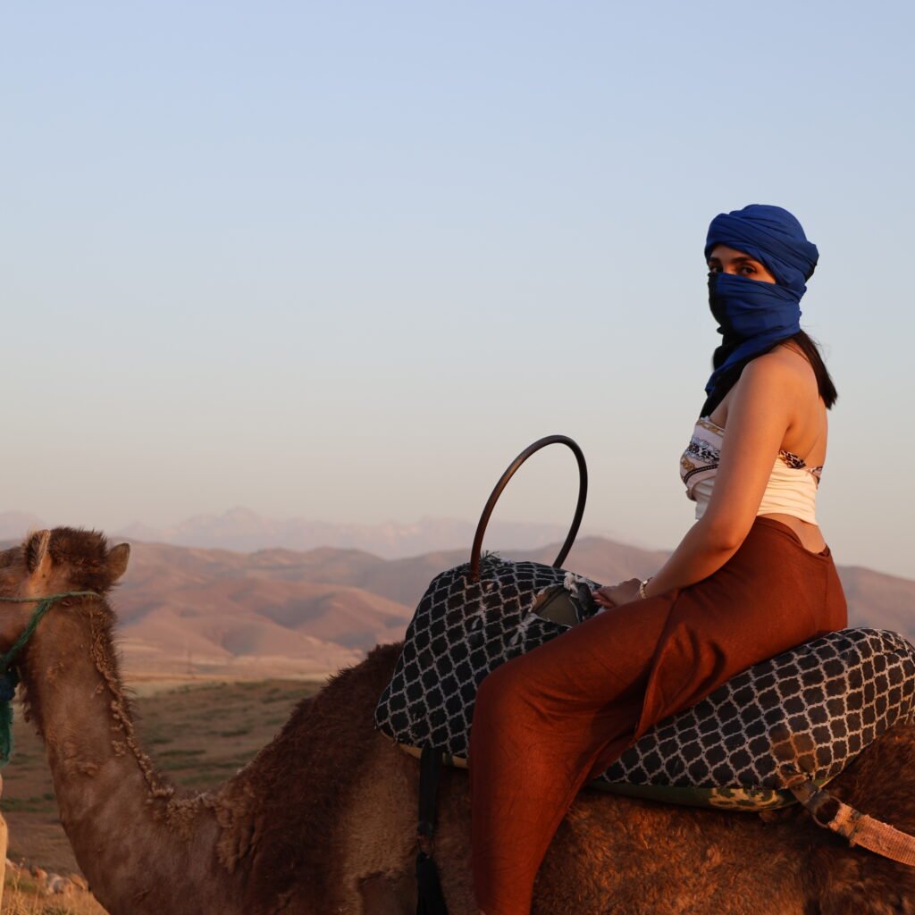 Female rider wearing a blue Tagelmust headwrap on a camel during a Moroccan desert excursion