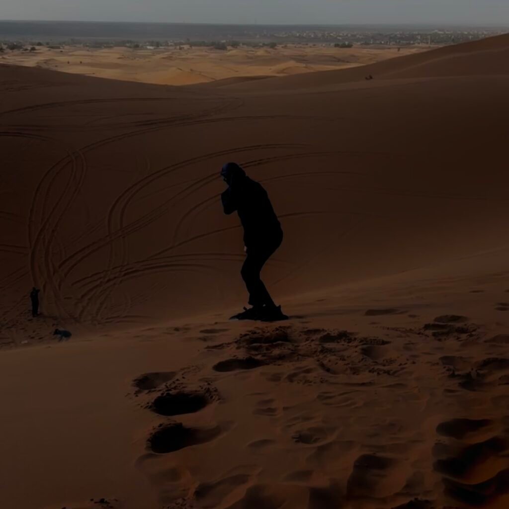 Silhouette of a sandboarder balancing on the crest of a desert sand dune