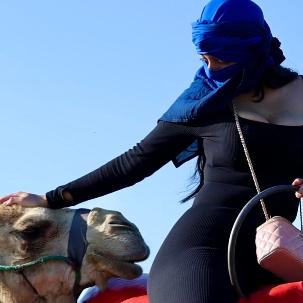 Female traveler in a blue headwrap gently petting her camel during a desert ride