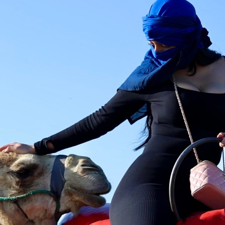 Female traveler in a blue headwrap gently petting her camel during a desert ride
