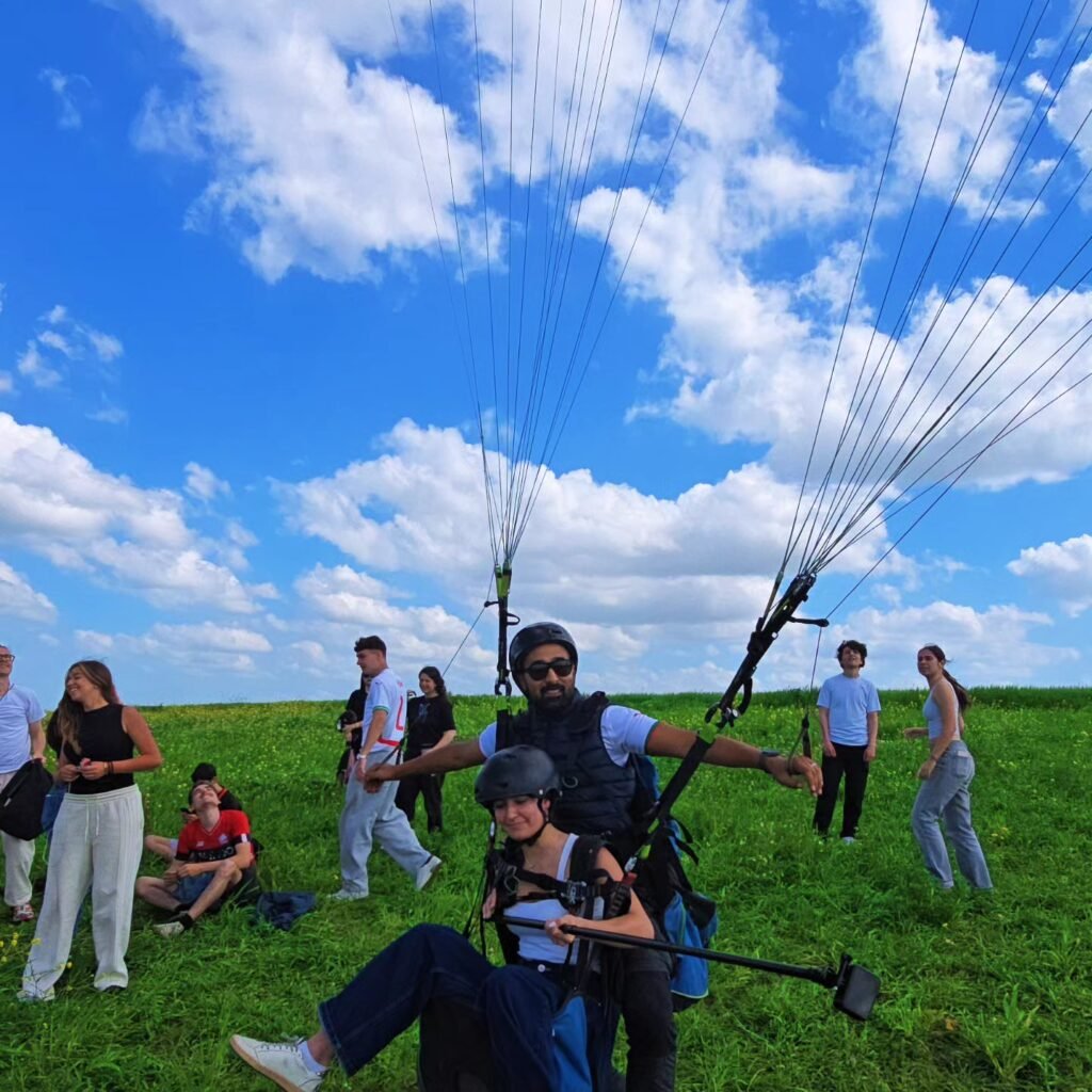 Travelers preparing for a tandem paragliding launch in a grassy meadow