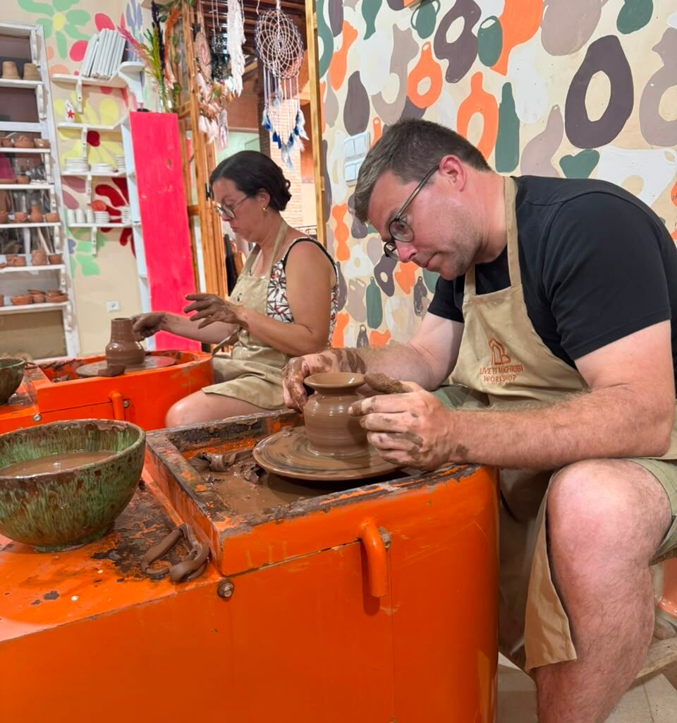 Travelers wearing aprons crafting clay pots on pottery wheels in a workshop