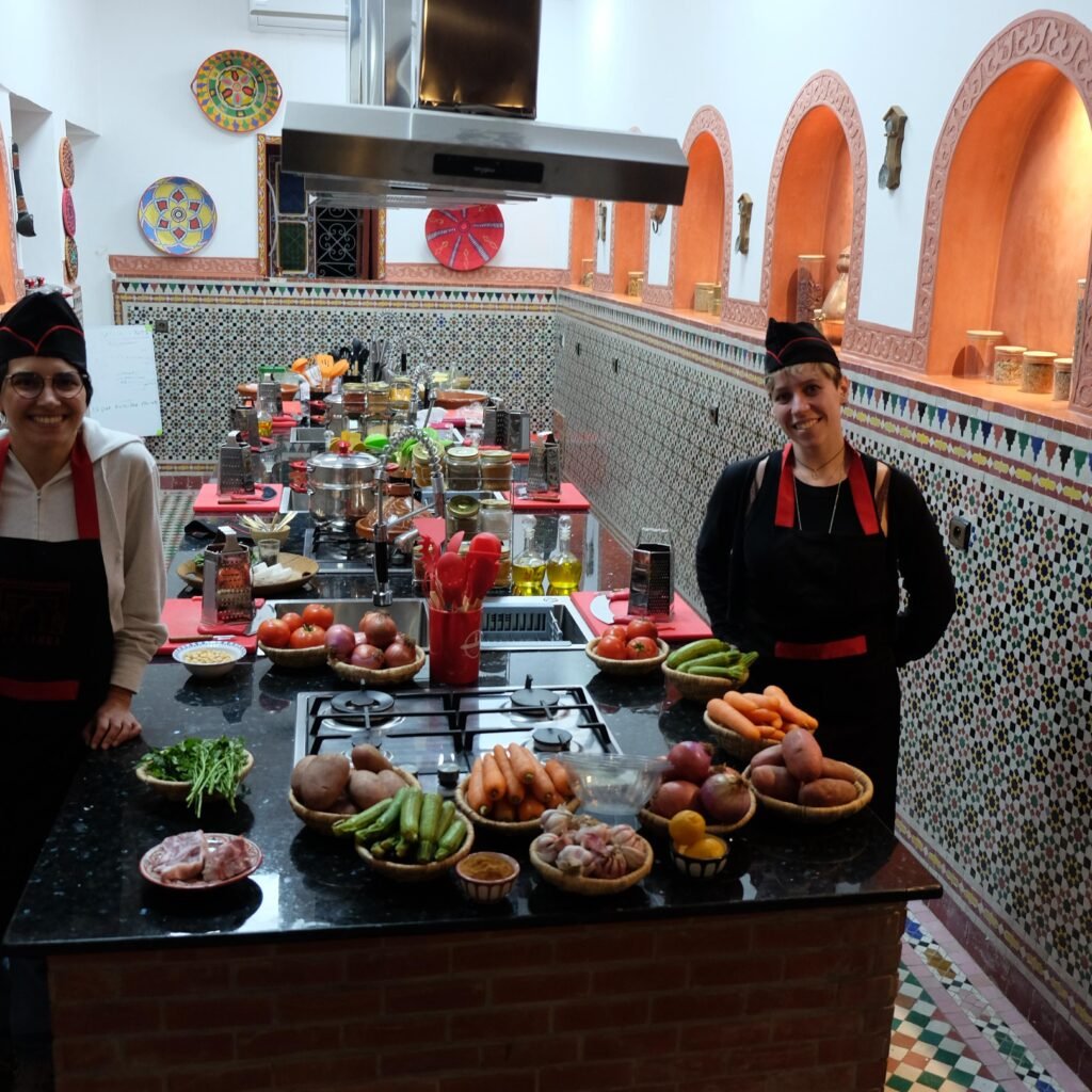 Two instructors standing by a kitchen island filled with fresh vegetables, meat, and cooking utensils