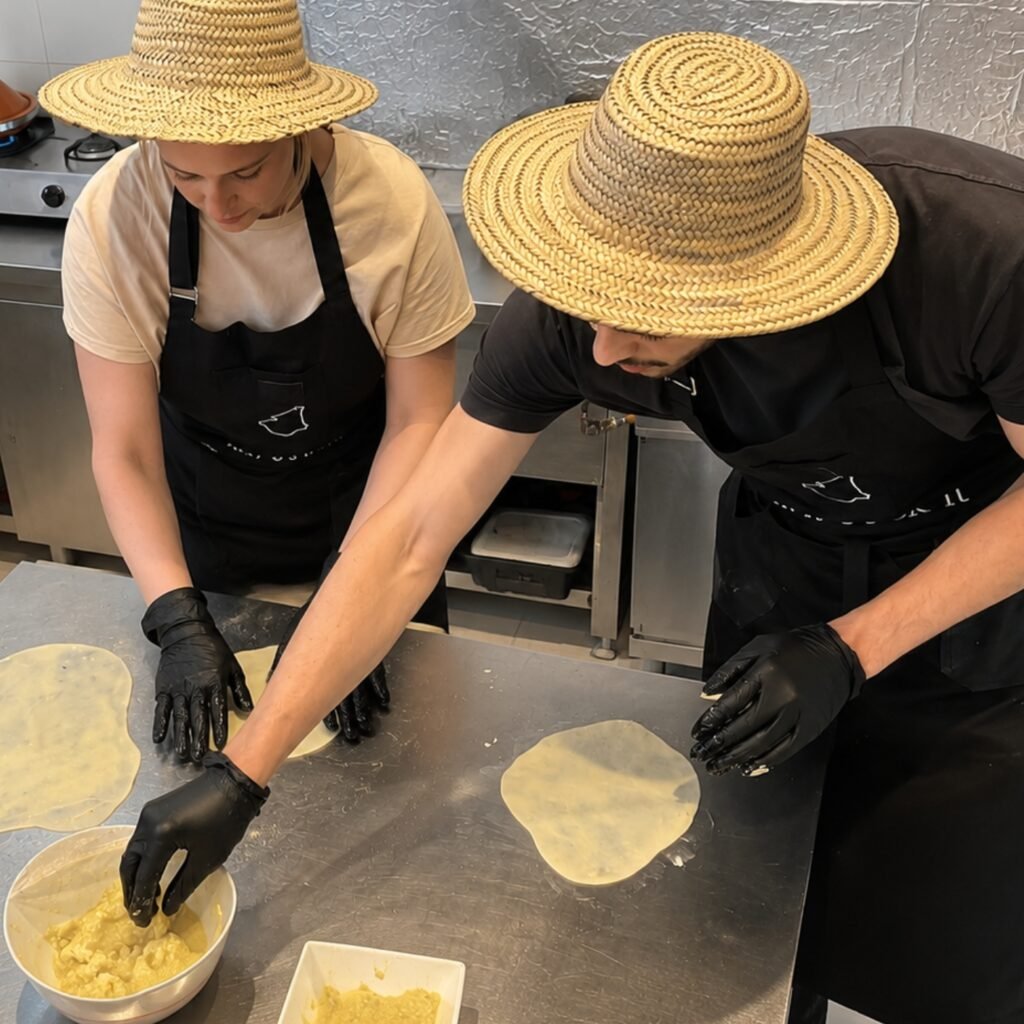 Travelers wearing straw sun hats making traditional Moroccan msemmen bread during a cooking class