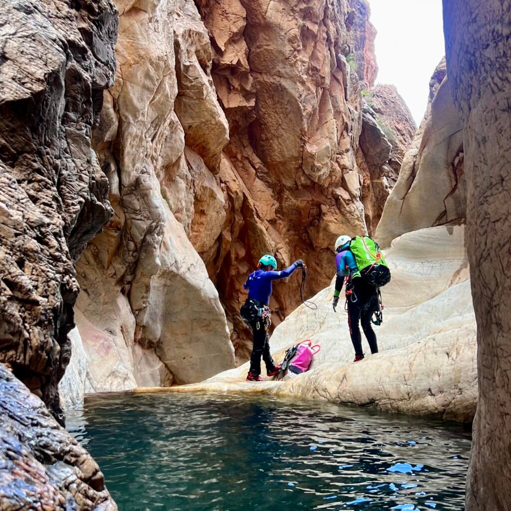 Canyoning participant gesturing thumbs-up while rappelling down a cliff above a natural river pool in Morocco