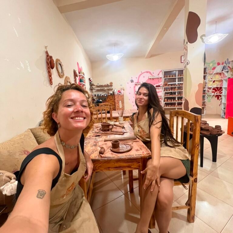 female travelers wearing aprons smiling together at a pottery workshop table
