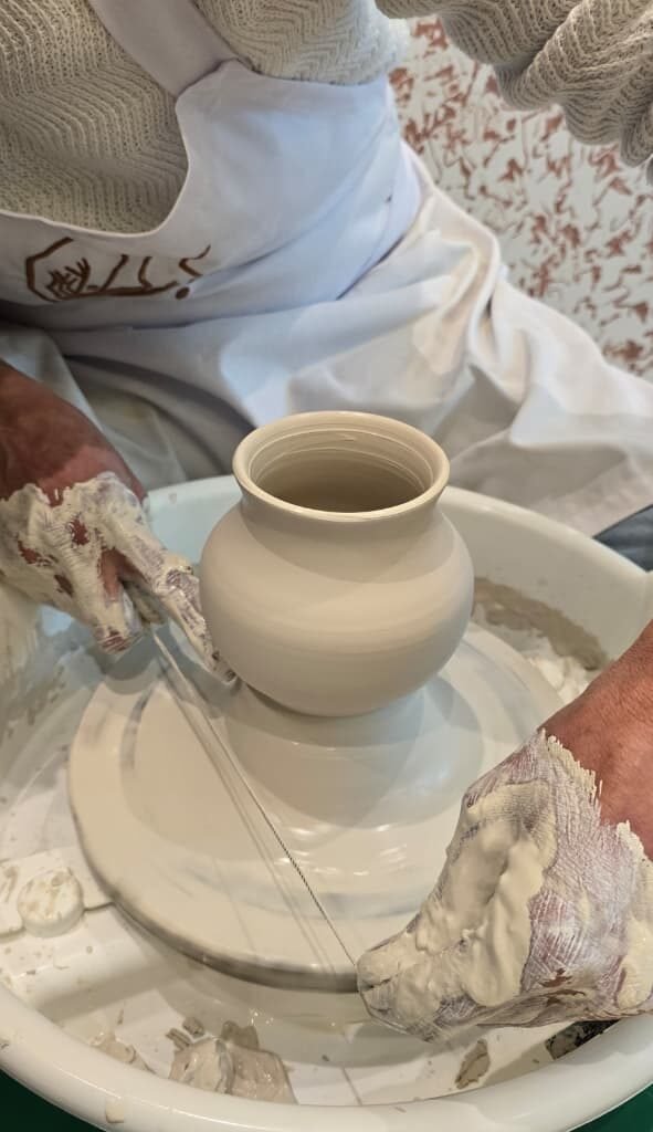 Potter using a cutting wire to detach a newly thrown ceramic pot from the wheel head