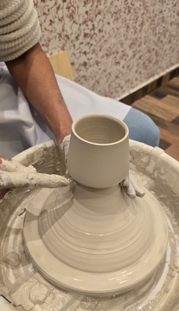 Potter shaping a small rounded vase on a spinning pottery wheel