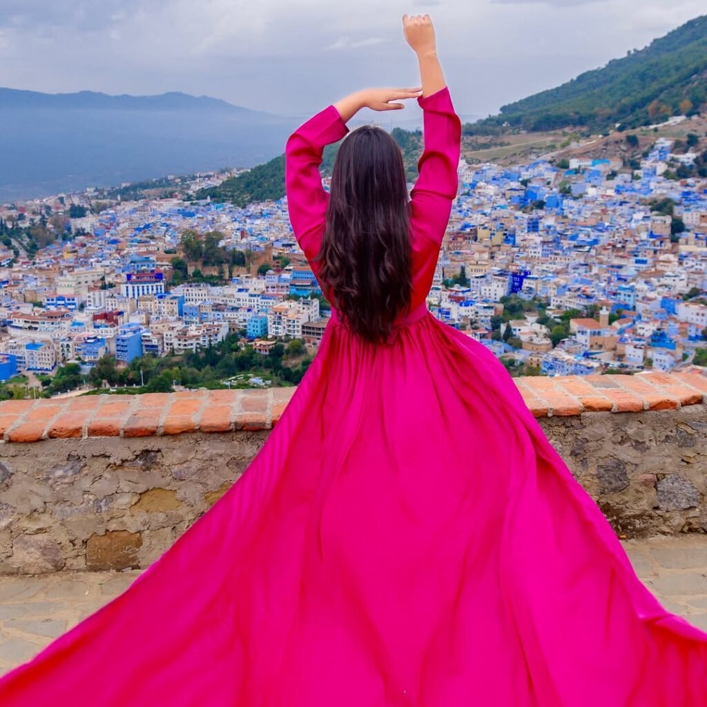 Traveler in a bright pink gown looking out over the blue city panorama of Chefchaouen, Morocco