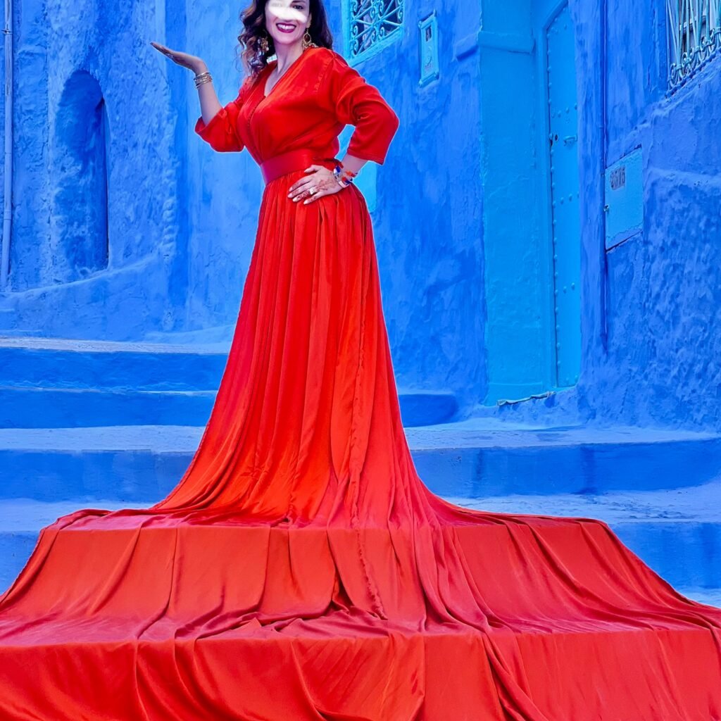 Woman in a vibrant red dress posing against blue-washed stone walls in Chefchaouen, Morocco