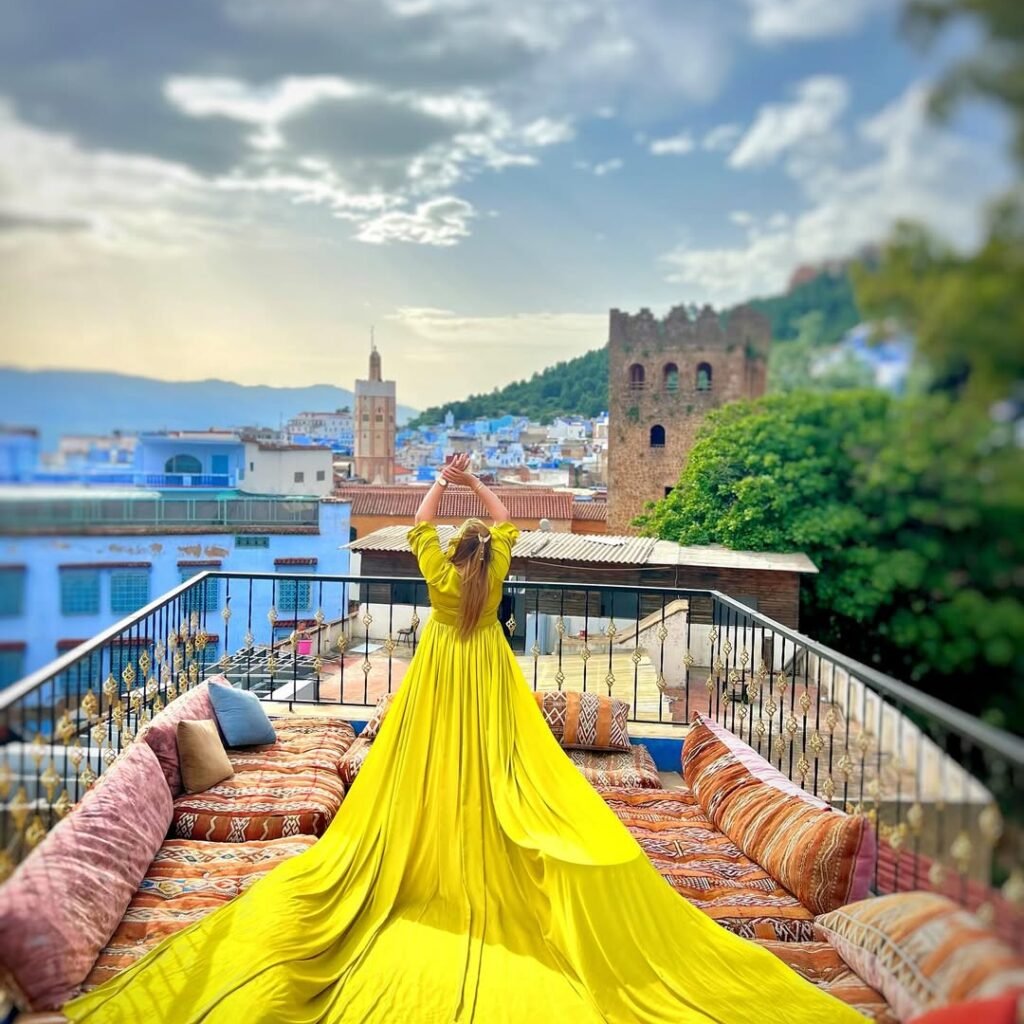 Woman in a bright yellow flying dress standing on a rooftop terrace overlooking Chefchaouen, Morocco