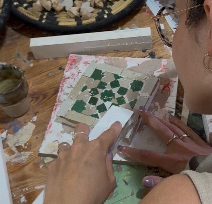 Close-up of a traveler applying grout to a green geometric zellij mosaic tile artwork