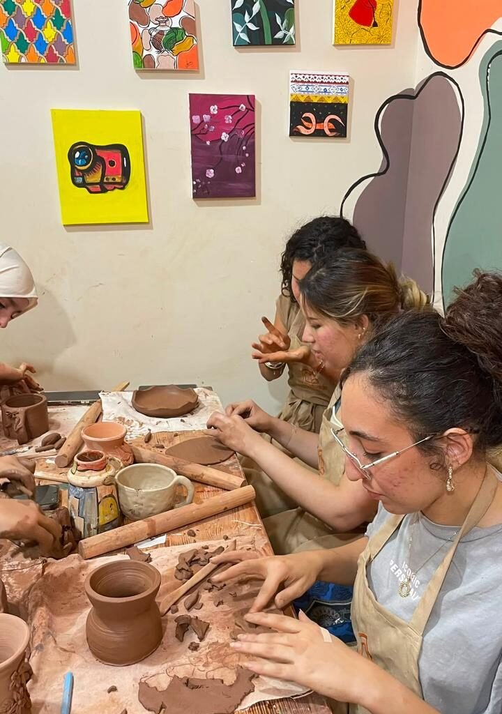 Group of female travelers sculpting clay items at a wooden table in a pottery class