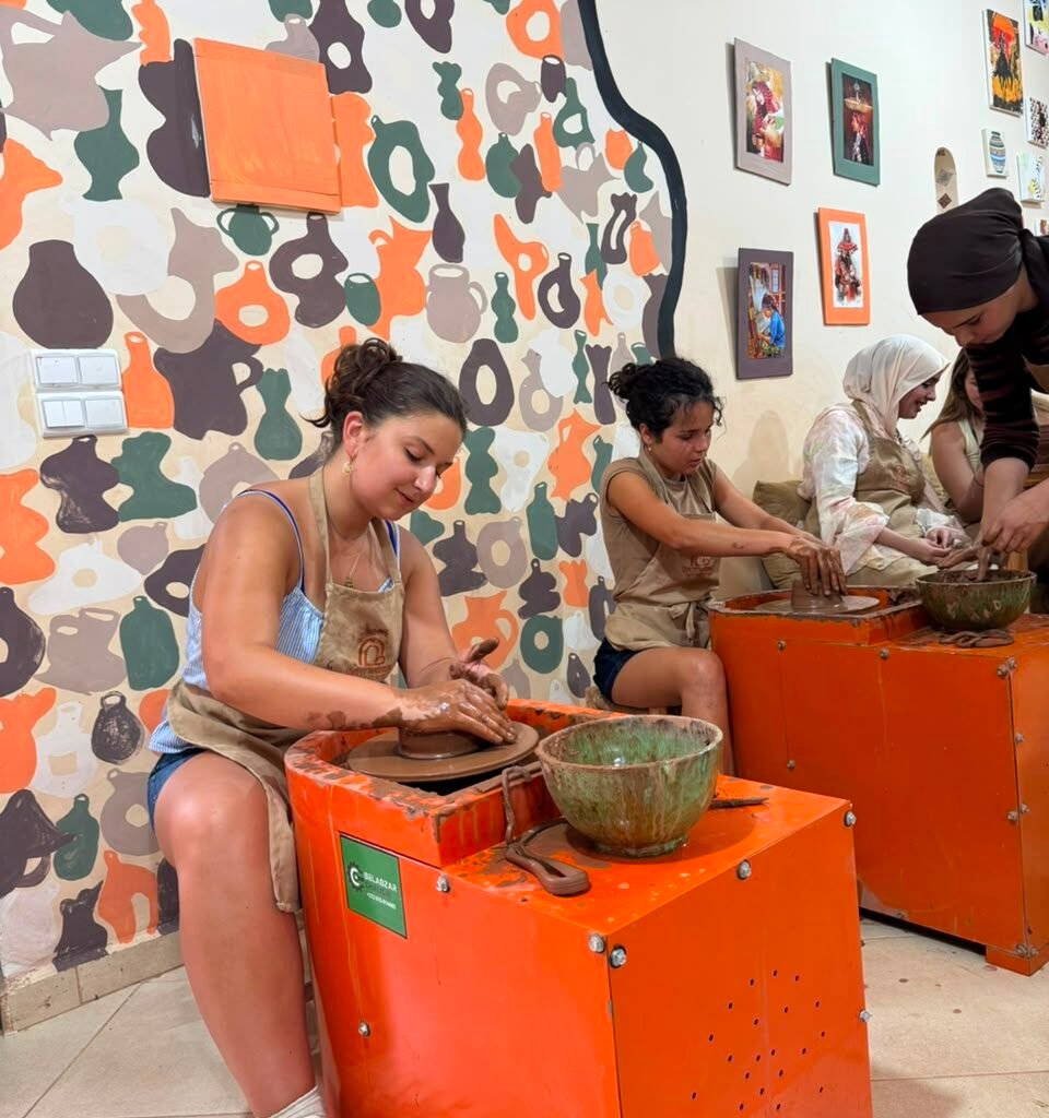 Young female travelers working on pottery wheels against a colorful patterned wall