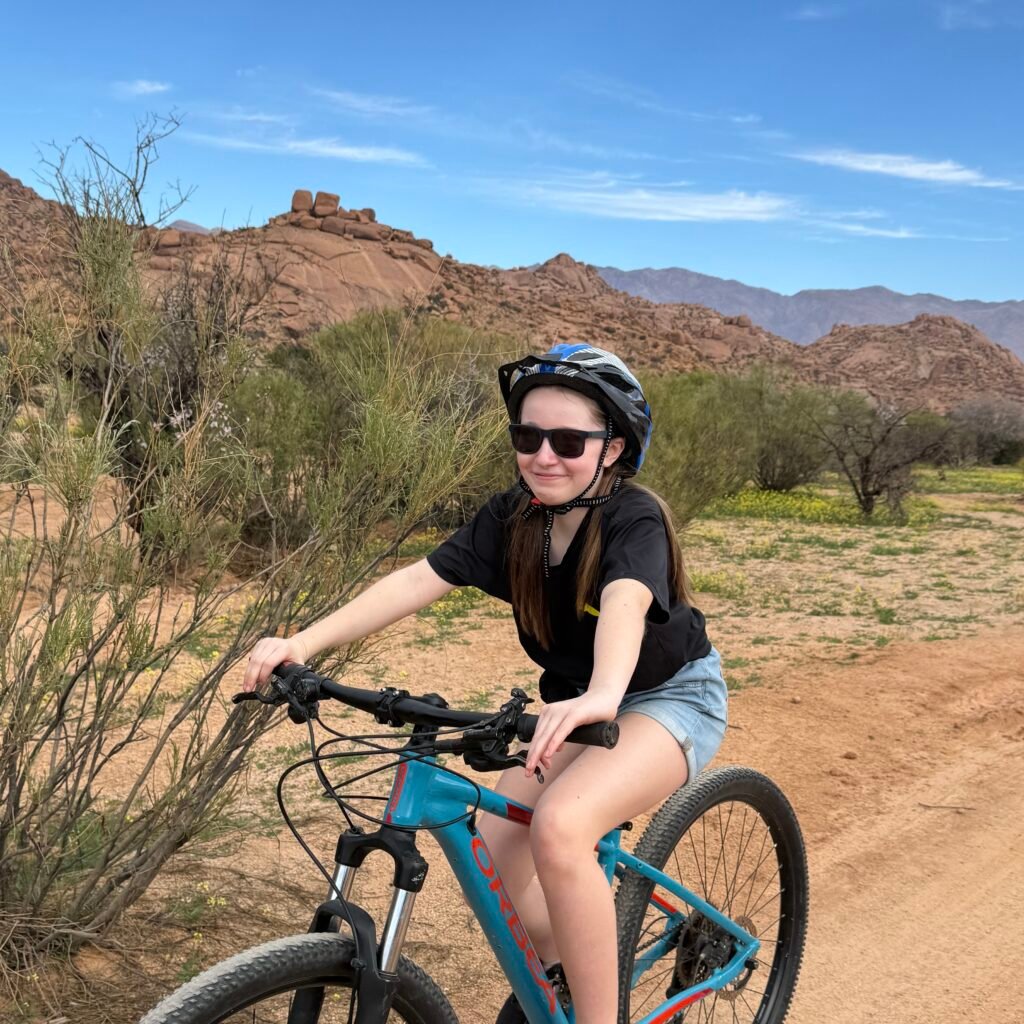 Young female traveler riding a blue mountain bike along a desert path near Tafraoute, Morocco