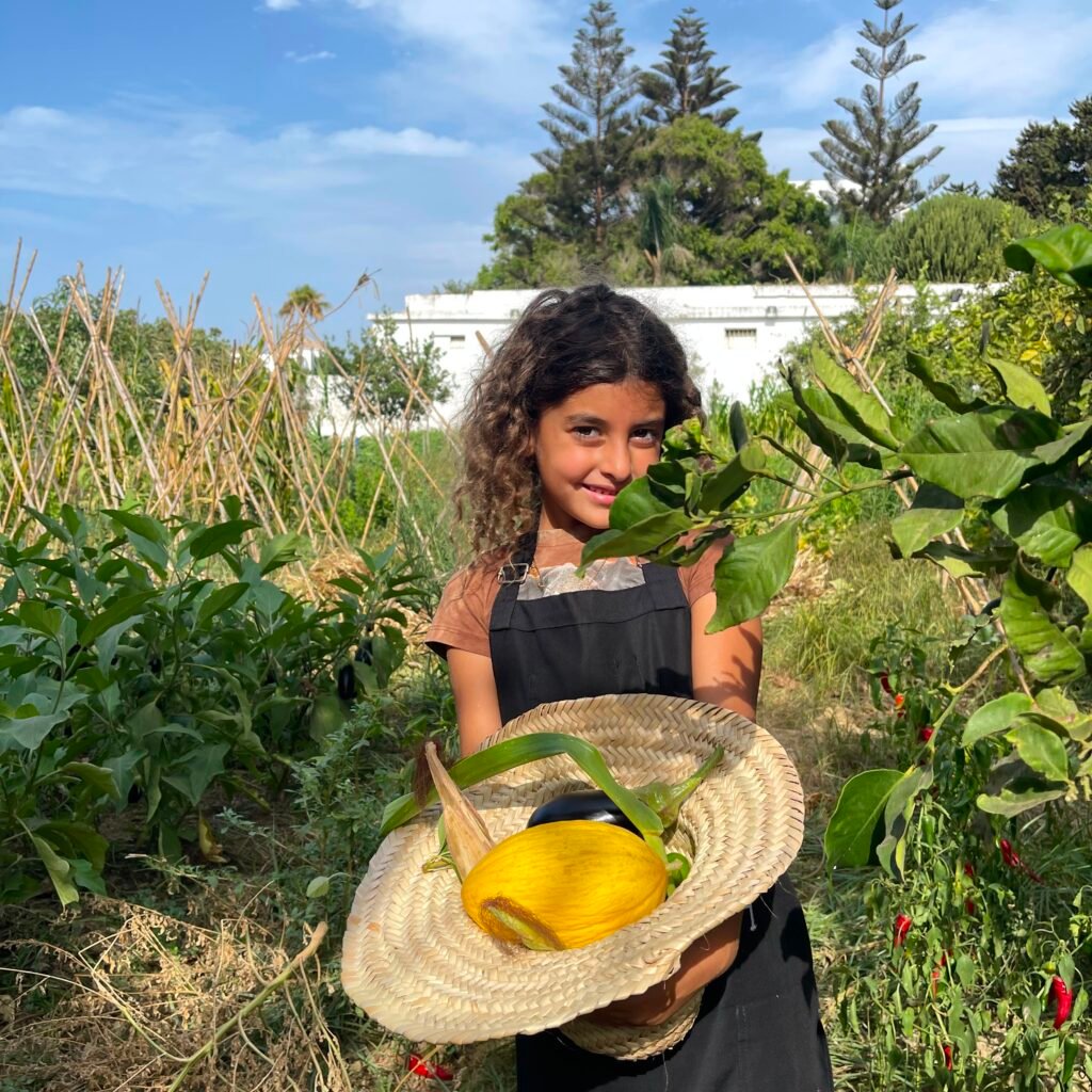 Young traveler holding a straw hat filled with harvested produce during an organic farm experience