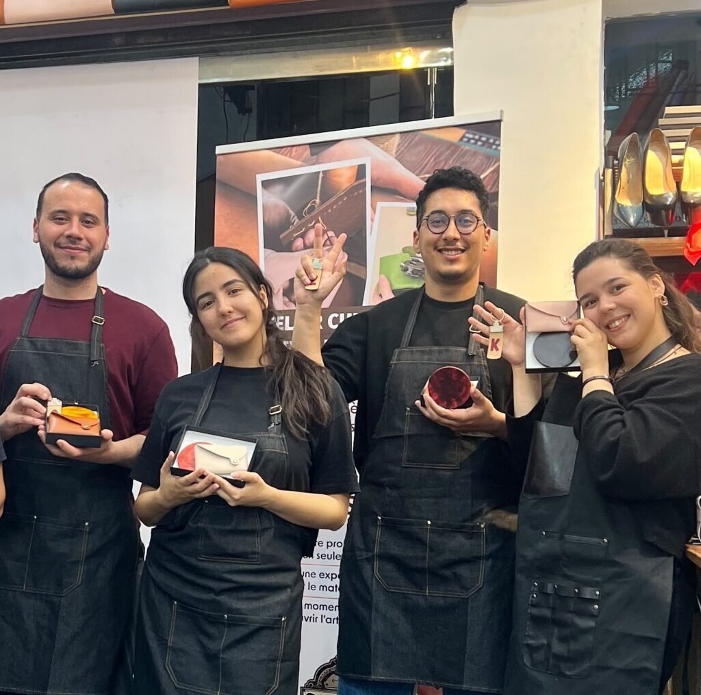 Five participants holding up their completed leather craft creations at an artisan workshop