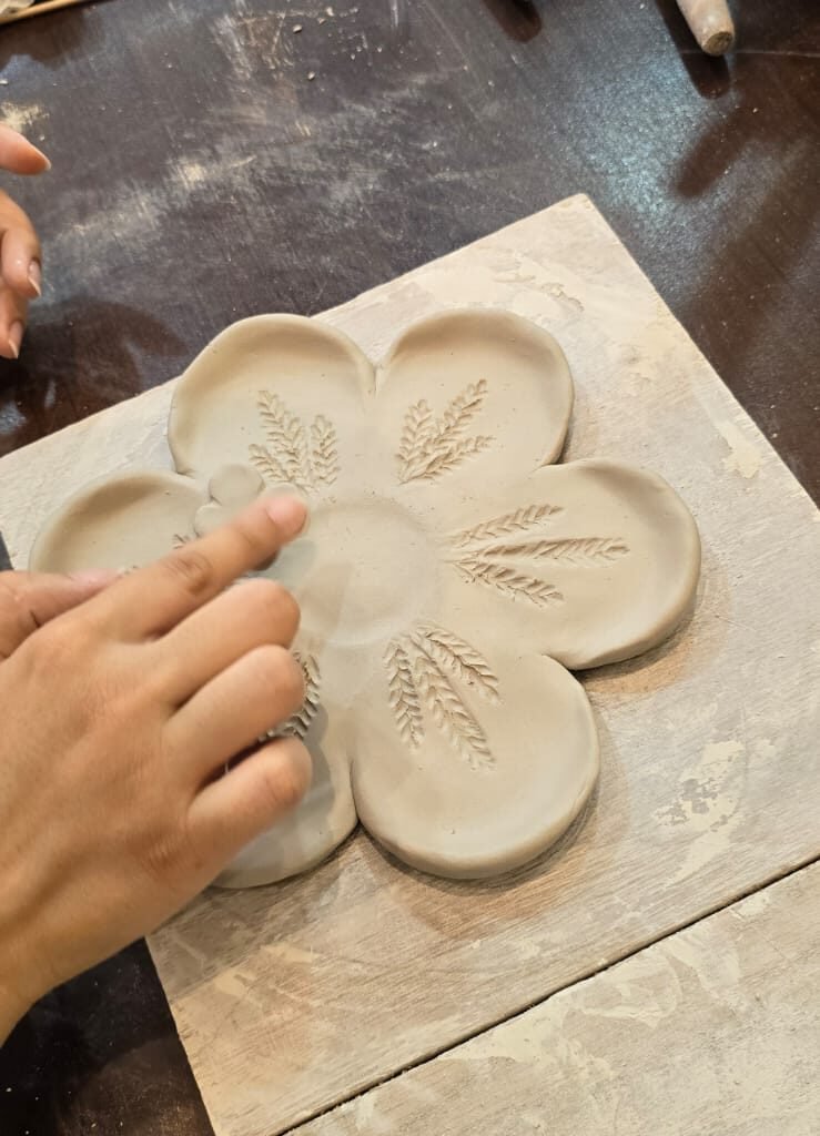 Person carving leaf details into the petals of a handmade clay flower dish